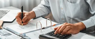 A person at a desk, using a calculator and writing in a notebook.