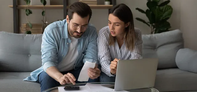 A couple sitting on a couch working on a laptop together.